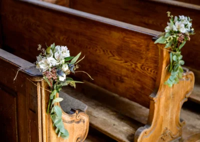 Blumenarrangement an Kirchenbank bei Hochzeit in St. Alban, Diessen am Ammersee. Romantische Details der Trauung.