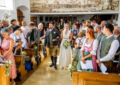Kirchliche Trauung in St. Alban Diessen, Brautpaar schreitet durch mit Gästen gefüllte Kirche in traditioneller Tracht.