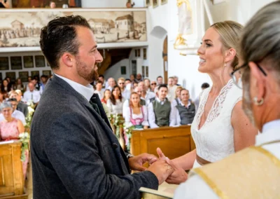 Brautpaar bei kirchlicher Trauung in St. Alban, Diessen am Ammersee, umgeben von Gästen in traditioneller Kleidung.