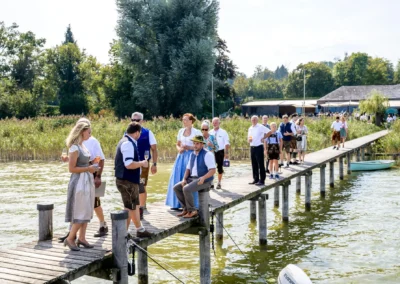 Hochzeitsgäste in Tracht auf einem Steg bei einer Feier im Seehaus Riederau am Ammersee. Hochzeit in Bayern.
