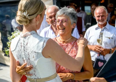 Braut begrüßt Gast bei Hochzeit in St. Alban, Diessen. Feier im Seehaus Riederau, Brautpaarshooting auf dem Steg.