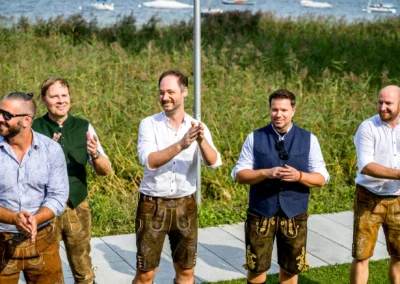 Hochzeitsgäste in Tracht applaudieren während einer Feier am Seehaus Riederau, Hochzeit in Diessen.