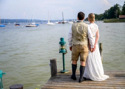 Brautpaar am Steg des Ammersees, Hand in Hand, im traditionellen Hochzeitsoutfit bei einer Hochzeitsreportage.