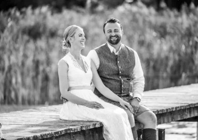 Lachendes Brautpaar auf Steg, Hochzeitsfotografie im Freien, romantisches Brautpaarshooting.
