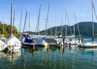 Brautpaar-Shooting am Bootssteg in Bad Wiessee, Tegernsee, mit Gebirgsblick und Segelbooten im Hintergrund.