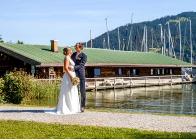 Brautpaar-Shooting am Tegernsee in Bad Wiessee, idyllische Kulisse aus Booten und Bergen im Hintergrund.