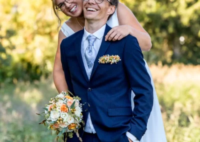 Brautpaar-Shooting am Tegernsee in Bad Wiessee, lachendes Paar mit Blumenstrauß, idyllische Hochzeitsmomente.