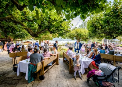 Hochzeitsfeier im Terrassenhof Bad Wiessee, Gäste unter Bäumen, abendliche Feier im Bootshaus.