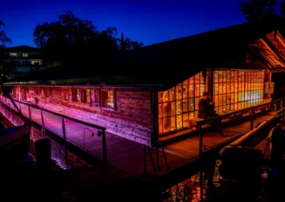 Hochzeitsfeier im Bootshaus des Terrassenhofs Bad Wiessee bei Abendstimmung, romantische Lichter spiegeln sich im Wasser.