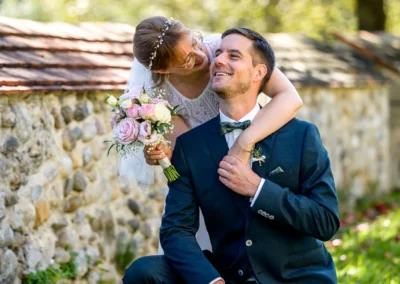 Brautpaar beim Fotoshooting in Pfaffing bei Ebersberg, lächelnd und glücklich im Garten mit Blumenstrauß.