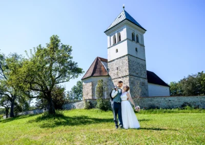 Brautpaar-Fotoshooting vor einer Kirche in Pfaffing bei Ebersberg an einem sonnigen Tag.