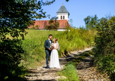 Brautpaar-Fotoshooting in Pfaffing bei Ebersberg, romantischer Spaziergang auf Landstraße vor Kirche.