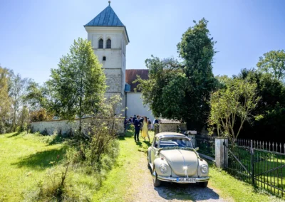 Kirchliche Trauung in St. Margaretha, Pfaffing: Oldtimer vor der Kirche, Brautpaar und Gäste im Hintergrund.