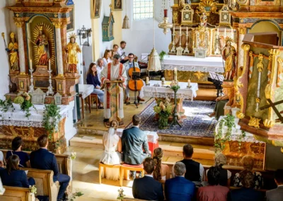 Kirchliche Trauung in St. Margaretha, Pfaffing: Brautpaar vor Altar, Gäste und Priester in feierlicher Atmosphäre.