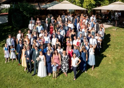 Hochzeitsfeier im Landgut Kugler-Alm, Ebersberg, mit Hochzeitsgesellschaft im Freien unter Sonnenschein. Gruppenfoto mit Drohne